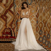 A floor-length A-line wedding dress with a deep V-neck, lace bodice, spaghetti straps, and a high slit.