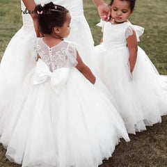 Two young girls wear white puffy ball gown flower girl dresses with lace appliques and sheer necks.