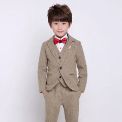 A young boy wears a tan tweed four-piece formal suit with a red bow tie and white shirt.
