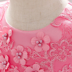 Close-up of a pink baby dress featuring floral embroidery and pearl-centered fabric flowers.