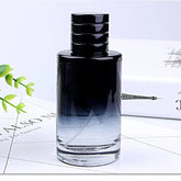 A cylindrical glass perfume bottle with a black gradient finish and a black cap.