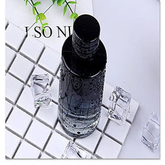 A black perfume bottle covered in water droplets sits on a white tiled surface with ice cubes.