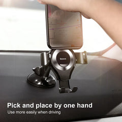 A black Baseus gravity car phone holder with a suction cup base mounted on a dashboard.