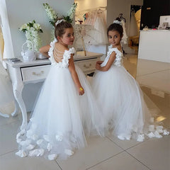 Two young girls wearing white floor-length ball gowns with beaded back detailing and floral accents.