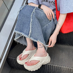 A pair of beige platform flip-flops with a thick, soft sole worn by a person on an escalator.