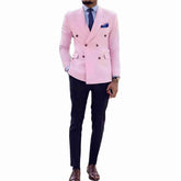 A man wears a slim-fit pink double-breasted suit with a peaked lapel and dark trousers.