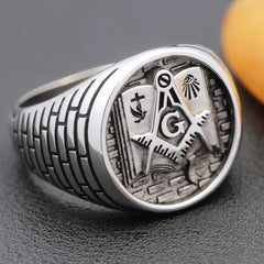 A sterling silver Masonic ring featuring a square and compass with a G on a brick-patterned band.