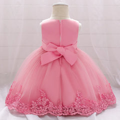 A sleeveless pink baby dress with a tulle skirt and floral lace hem, featuring a back bow.
