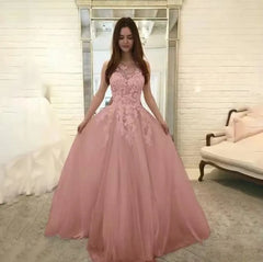 A woman wears a sleeveless, floor-length dusty pink tulle ball gown with a lace bodice.