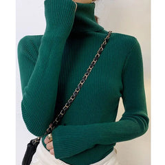 A woman wears a slim-fit, long-sleeved dark green turtleneck sweater with a ribbed texture.