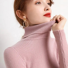 A woman wears a soft, pink, slim-fit turtleneck sweater with long sleeves.
