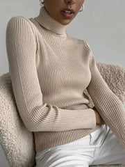 A woman wears a beige, slim-fit, ribbed turtleneck sweater with long sleeves.