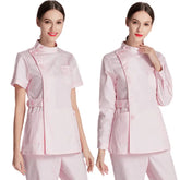 A woman models a light pink medical scrub uniform with a button-up tunic and matching trousers.