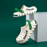 A pair of white EVA clogs with green straps and the word DREAM printed on the side.