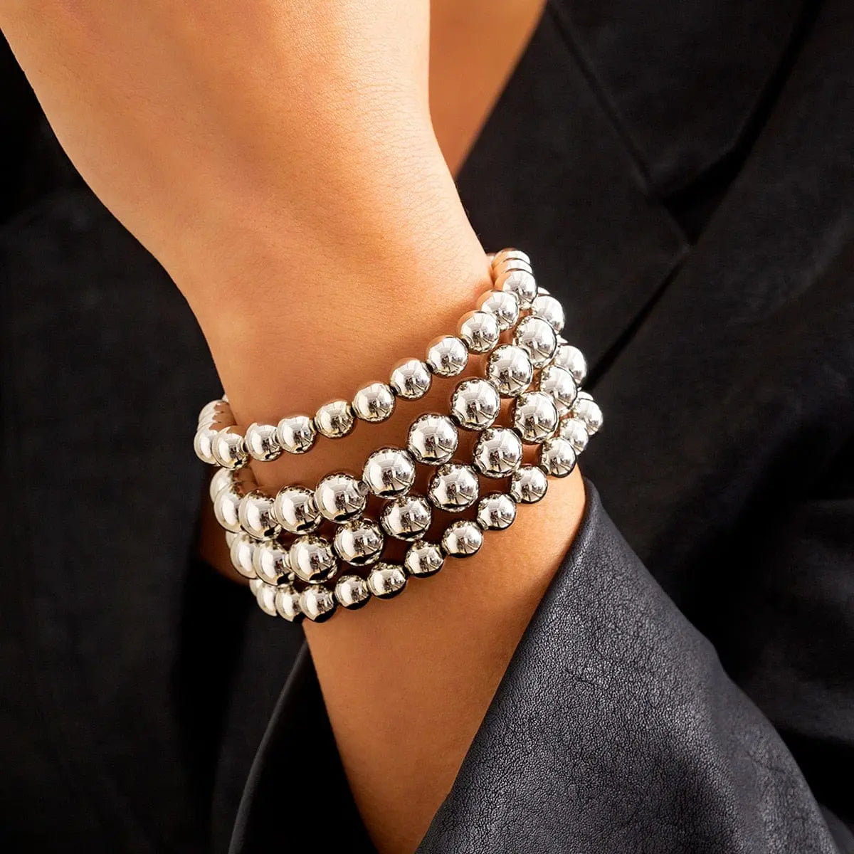 A person wears a multi-layered bracelet made of large, shiny silver-toned plastic beads.