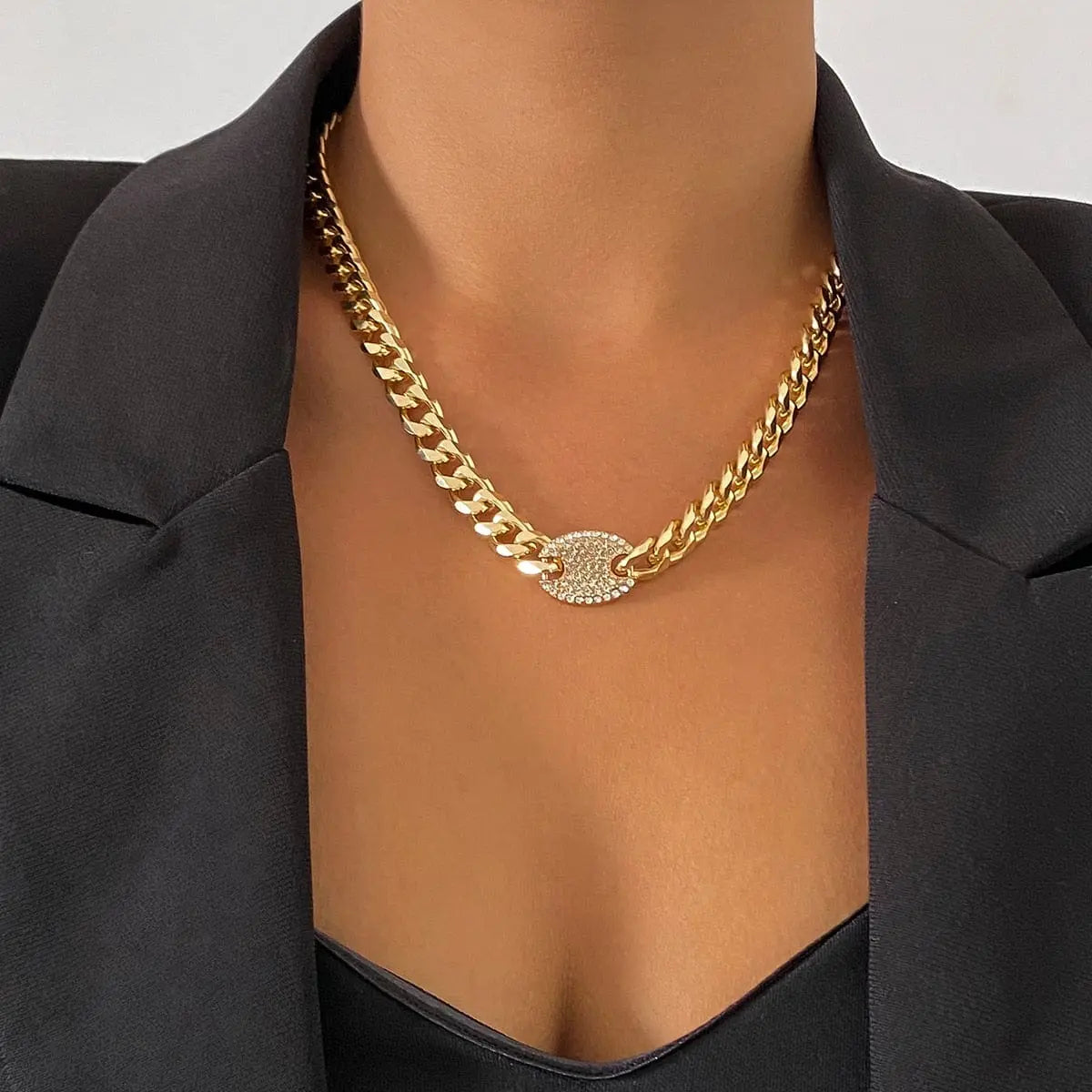 A person wearing a black blazer and the Ingemark Iced Out Rhinestones Tennis Chain Pendant Choker Necklace, featuring a round, diamond-studded pendant. The background is plain and light-colored.