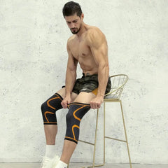 A man sits on a stool wearing black and orange compression knee pads for sports support.