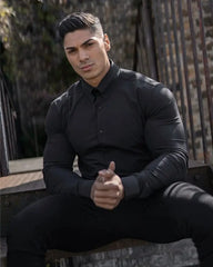 A man wears a slim-fit, long-sleeve black button-down shirt with a square collar.