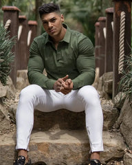 A man wears a slim-fit, long-sleeved olive green button-down shirt with a square collar.