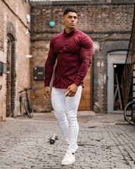 A man wears a slim-fit, long-sleeved burgundy button-down shirt with a square collar.