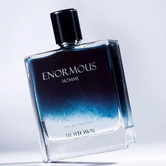 A glass bottle of Enormous Homme eau de toilette featuring a blue to clear gradient design.