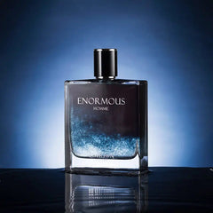 A rectangular glass bottle of Enormous Homme perfume with a dark blue gradient and glitter effect.