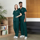 A man and a woman wearing matching dark green scrub sets with pink pocket accents.
