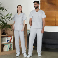 A man and a woman wearing matching light gray scrub sets with pink trim details.