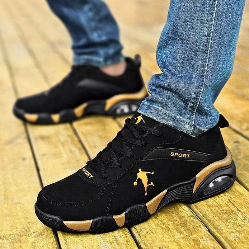 A person in blue jeans stands on a wooden floor, wearing Men's Sneakers 2022 New Lightweight Vulcanized Shoes—black and gold, anti-skid, breathable, and stylish with a basketball player silhouette design.