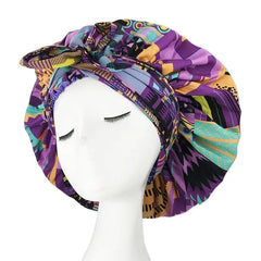 A mannequin head displays the New African Ankara Pattern Satin Lined Bonnet, a big-size, double-layer headscarf with long ribbon, in vibrant purple, yellow, teal, and black geometric patterns—ideal as a multifunctional hair cover.