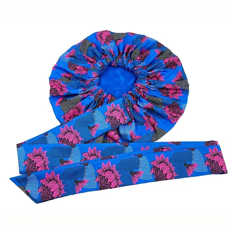 The New African Ankara Pattern Satin Lined Bonnet is a blue headscarf for women with pink and black floral designs, wavy lines, an attached long ribbon headwrap, double layers, and big adult-size hair cover.