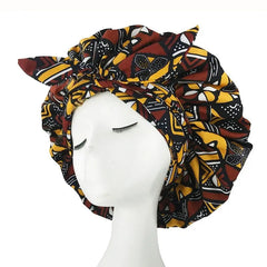 A mannequin displays the New African Ankara Pattern Satin Lined Bonnet—a big, double-layer headscarf with a red, yellow, black, and white geometric design and knotted front. Perfect as a floral headwrap or multifunctional hair cover.