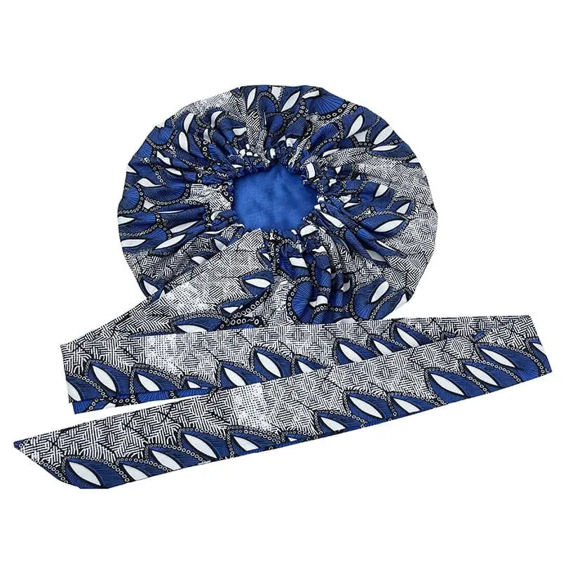 The New African Ankara Pattern Satin Lined Bonnet is a double-layer, big-size women’s headscarf featuring a blue, white, and black floral print outside, a solid blue interior, and an attached long ribbon headwrap for secure styling.