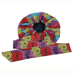The New African Ankara Pattern Satin Lined Bonnet features a colorful floral design in red, yellow, purple, and blue, paired with a matching ribbon headwrap. Both are double-layered for women and displayed on a white background.