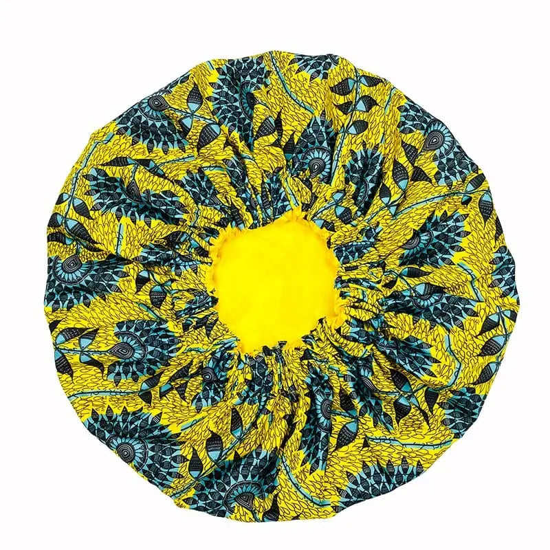 The New African Ankara Pattern Satin Lined Bonnet features a bright yellow center and blue-black fish and leaf print on yellow fabric, perfect as a multifunctional skull cap or floral headscarf. Double layered with long ribbon for adults.