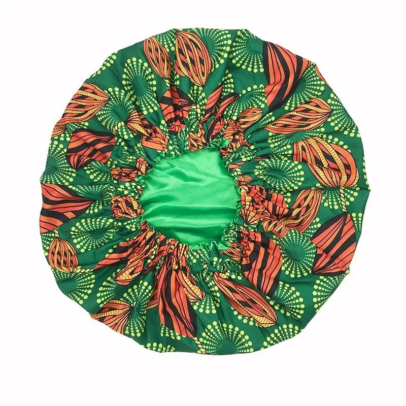 The New African Ankara Pattern Satin Lined Bonnet is a big-size, double-layer headscarf for women with a green base, vibrant orange, yellow, and black African-inspired pattern, long ribbon headwrap, and comfortable elastic edging.