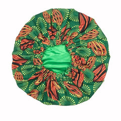 The New African Ankara Pattern Satin Lined Bonnet is a big-size, double-layer headscarf for women with a green base, vibrant orange, yellow, and black African-inspired pattern, long ribbon headwrap, and comfortable elastic edging.