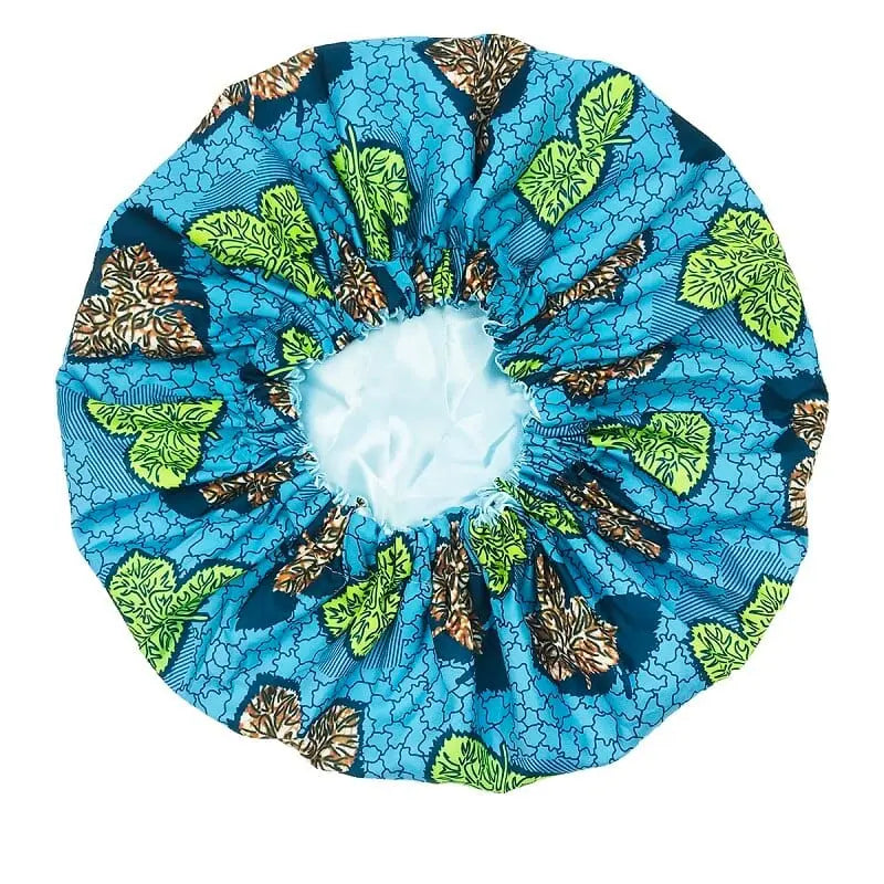 The New African Ankara Pattern Satin Lined Bonnet is a big-size women’s headscarf with green and brown leafy designs, black outlines, and an elastic band. It features a long ribbon and double-layer satin lining, shown on a white background.