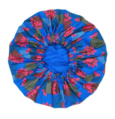 The New African Ankara Pattern Satin Lined Bonnet is a big size women’s headwrap with double layers, long ribbons, and vibrant pink and green floral patterns on blue fabric, gathered at the center with elastic for a secure fit.