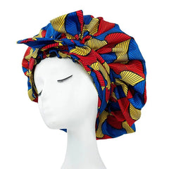 A mannequin displays the New African Ankara Pattern Satin Lined Bonnet, a bold geometric headwrap in red, yellow, and blue. This big size double layer headscarf features a gathered edge for versatile use as a skull cap or women’s beanie.