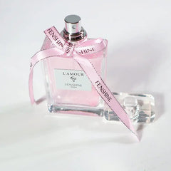 A rectangular glass perfume bottle filled with pink liquid and tied with a branded pink ribbon.