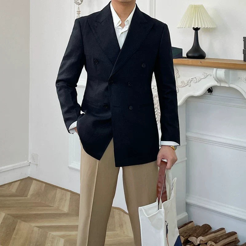 A man wears a slim-fit black double-breasted linen suit jacket with tan trousers.