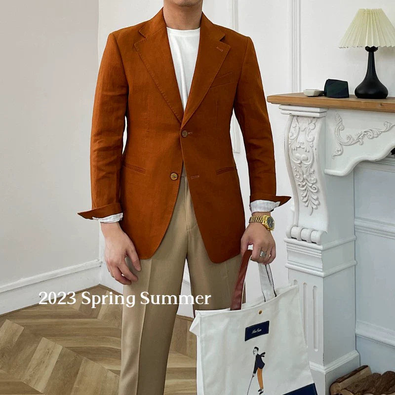 A man wears a rust-colored linen blazer over a white t-shirt and tan trousers.