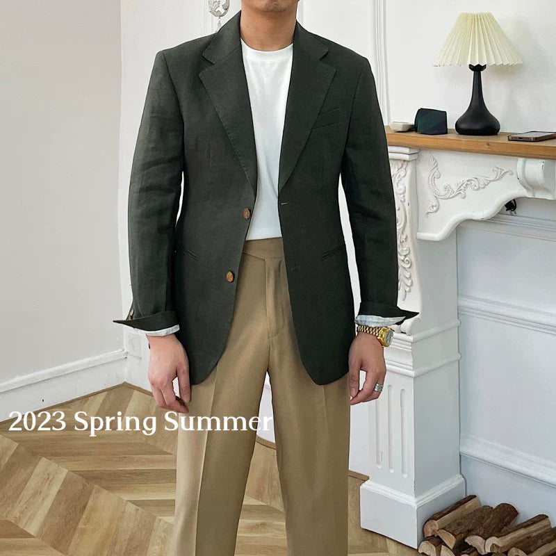 A man wears a dark green linen double-breasted blazer over a white t-shirt and tan trousers.