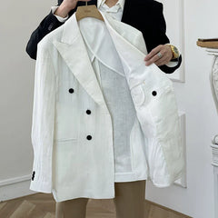 A white double-breasted linen suit jacket with black buttons held up by a person.