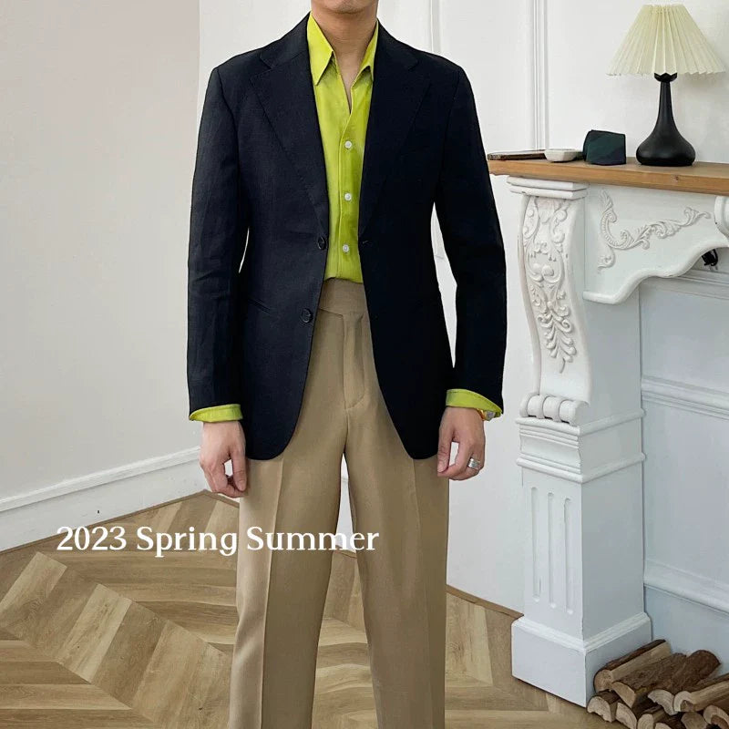 A man wears a black linen blazer over a lime green button-down shirt and tan trousers.