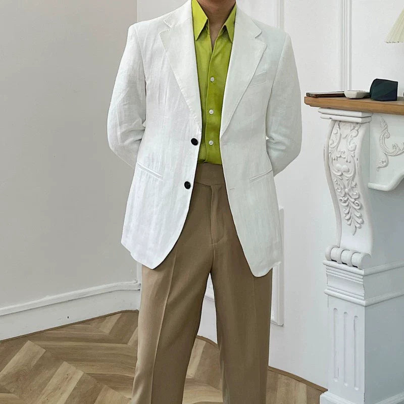 A man wears a white linen blazer over a lime green button-down shirt and tan trousers.