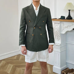 A man wears a dark green double-breasted linen suit jacket with white shorts.