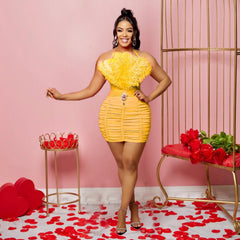 A woman wears a yellow sleeveless tube top mini dress featuring a feathered bodice and ruching.