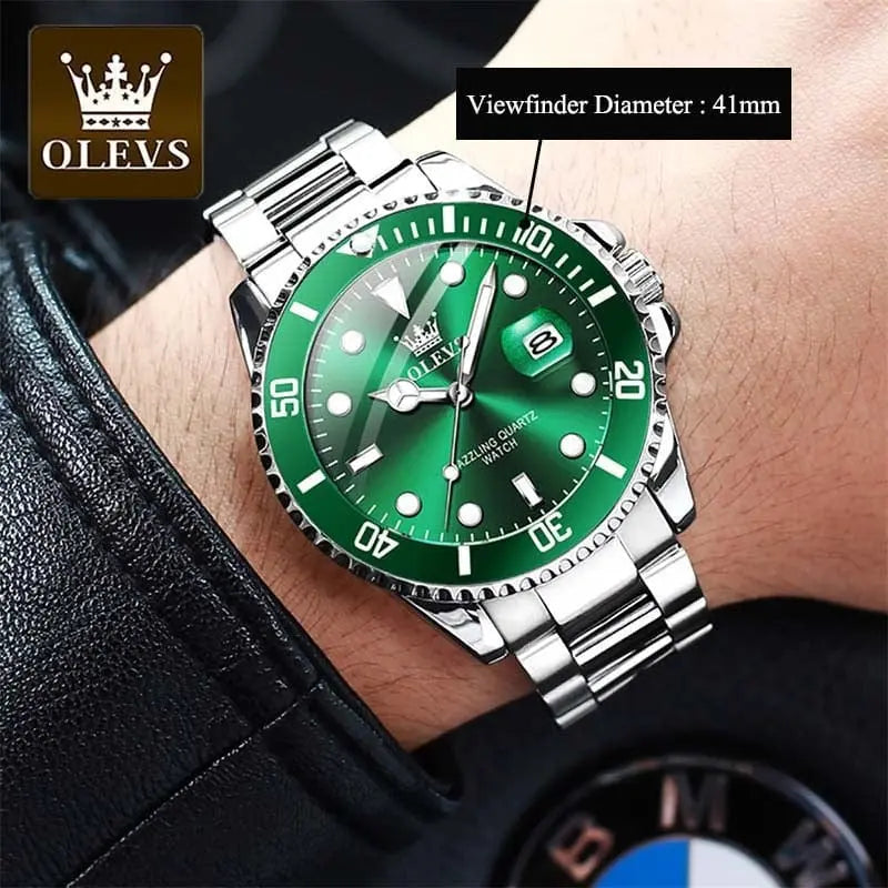A person wears a black leather sleeve and an OLEVS Mens Quartz Watch—top brand luxury, waterproof, luminous, with a silver case, green bezel and dial, large hour markers, date window, stainless steel band, and a 41mm viewfinder.